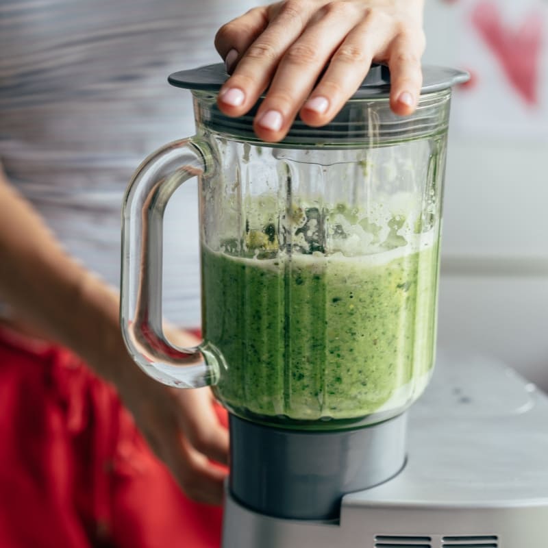 Woman blending a fresh green smoothie in a kitchen using a countertop blender ā perfect for healthy recipes.